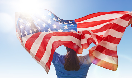 woman holding the American flag while looking up at the sky
