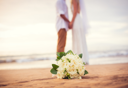 Married couple on the beach with flowers in the sand in the foreground